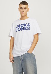 Tricou din bumbac alb cu imprimeu mare albastru "JACK & JONES" pe partea din față. Croi lejer, cu mâneci scurte. Purtați cu blugi deschiși.