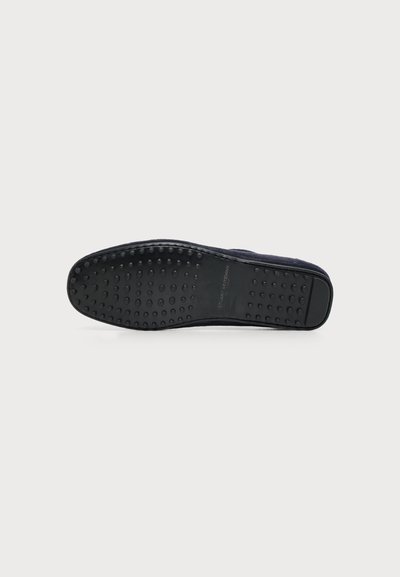 Semelle noire d'un mocassin de conduite pour homme avec des picots en caoutchouc surélevés pour l'adhérence, présenté sur un fond gris clair uni.