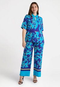 Completo a due pezzi composto da un top a maniche corte con colletto e pantaloni larghi, entrambi in un blu vivace con motivi floreali e accenti a contrasto.