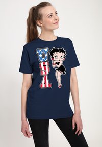 Námorně modré tričko s vintage kreslenou postavičkou "Betty Boop" vedle nápisu "USA" v tučných červených a modrých písmenech s hvězdicovými detaily.