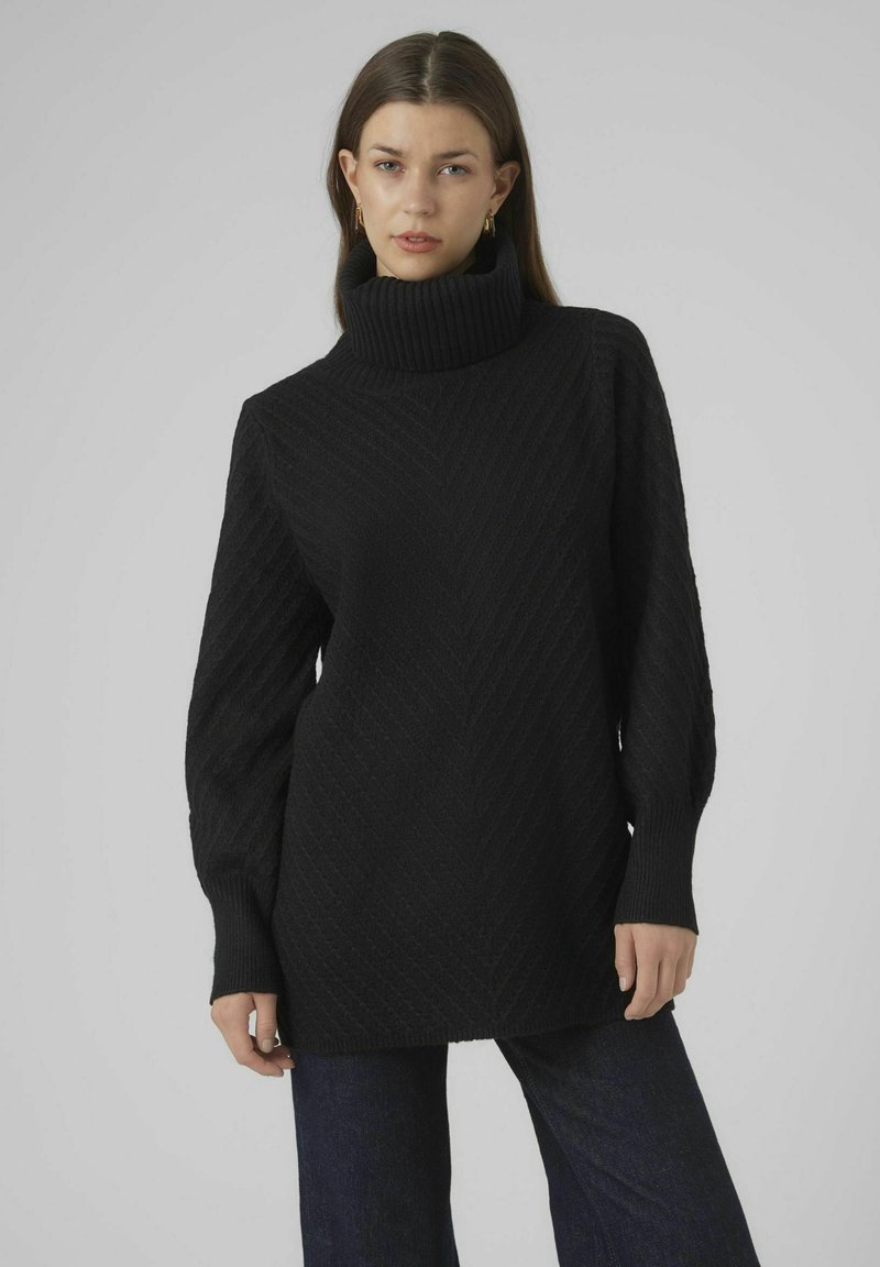 Maglione nero a treccia con collo alto e maniche ampie, caratterizzato da un motivo testurizzato e una vestibilità rilassata, abbinato a jeans scuri.