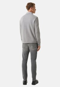 Grijze gebreide trui met een kraagontwerp, gecombineerd met grijze slim-fit jeans en zwarte schoenen. De textuur lijkt zacht en glad.