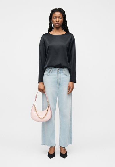 Γυναίκα που φοράει μαύρο μακρυμάνικο μπλουζάκι, ανοιχτό μπλε τζιν παντελόνι με φαρδιά μπατζάκια, μαύρες μυτερές γόβες, κρατώντας ροζ τσάντα με χρυσή αλυσίδα.