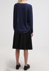 Navy modrá dlouhá halenka s uvolněným střihem, splývavou zadní částí, spárovaná s černou sukní do kolen a černými nazouvacími botami. Hladký materiál.