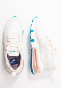 Bílé tenisky Nike Air s růžovými a modrými akcenty, jedna bota z pohledu shora a druhá z bočního pohledu na bílém pozadí.