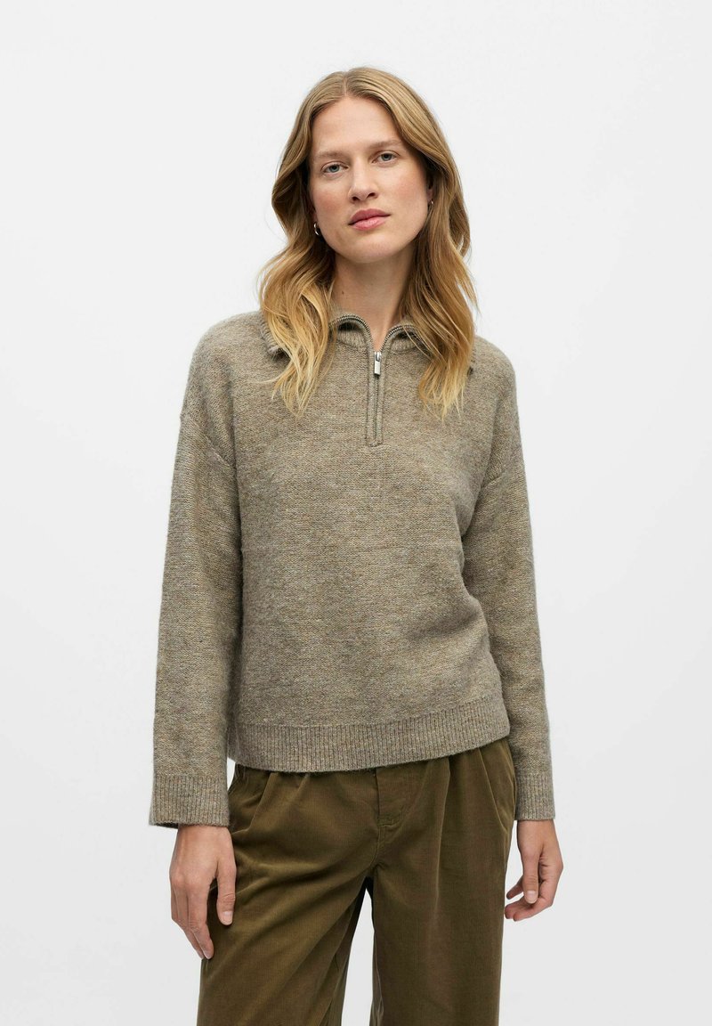 Heled pruun, tekstureeritud kudumiga pullover-sviiter, millel on pool-kinnituskaelus, soonikkoes varrukad ja äär. Koos oliivroheliste pükstega.