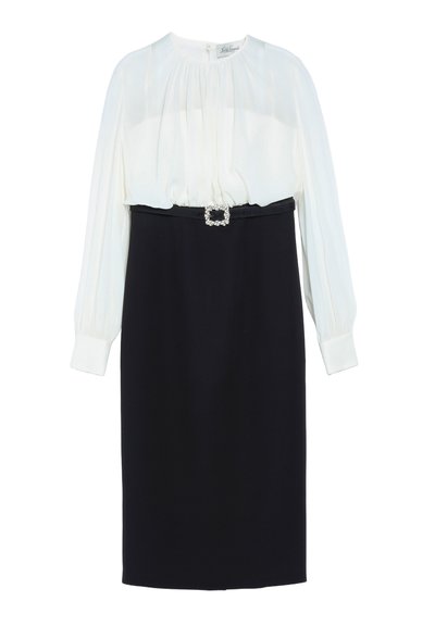 Robe à manches longues avec un haut blanc plissé, une jupe noire ajustée et une ceinture noire avec une boucle carrée en strass à la taille.
