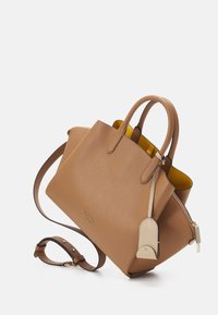 Torebka Kate Spade w kolorze brązowym z podwójnymi uchwytami, odpinanym paskiem na ramię, złotym zamkiem i beżową metką skórzaną na białym tle.
