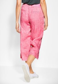 Růžové lněné culottes s uvolněným střihem, vybavené postranními a zadními kapsami, a mírně texturovaným povrchem; nošeny s bílými teniskami.