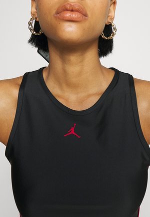 Zbliżenie osoby noszącej czarny bezrękawnik z małym czerwonym logo Jumpman i złotymi kolczykami w kształcie kół.