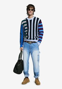 Pruhovaný sveter v rôznych farbách s modrými, námorníckymi a burgundskými akcentmi; rifle svetlej farby; hnedé topánky; nesie čiernu tašku.