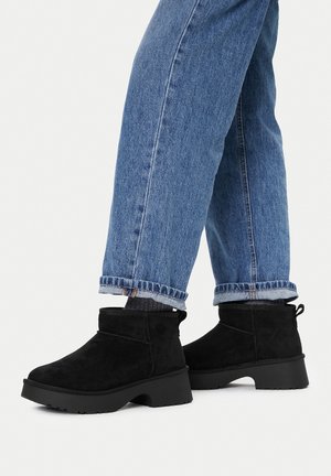 Person wearing cuffed blue jeans and black suede ankle boots with thick soles on a white background.