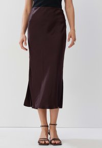 Satinbrauner Midirock mit taillierter Passform und seitlichem Schlitz, glatte Textur, kombiniert mit braunen Riemchensandalen.