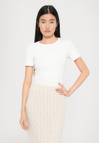 Haut ajusté blanc à manches courtes associé à une jupe crayon beige clair avec des motifs ondulés texturés et une taille haute.