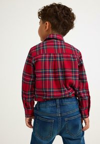 Rød ternet skjorte med grønne og gule detaljer, knapmanchetter og en lige rygdesign, parret med blå denimjeans.