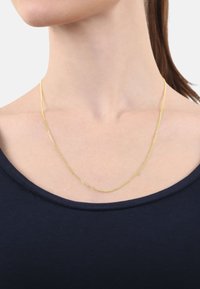 Collar de cadena de oro con un diseño suave y delicado, que presenta una textura sutil. Lleva puesto sobre una blusa de cuello redondo de color azul oscuro.