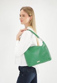 Groene leren handtas met zilveren studs langs één kant, voorzien van een korte schouderband en een zachte textuur.