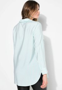 Camisa azul claro con rayas verticales, de mangas largas y con puños abotonados. Presenta un cuello y un dobladillo redondeado. Textura suave.