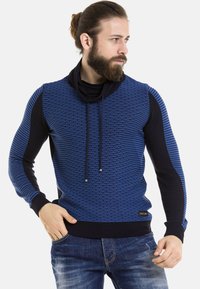 Blauer strukturierter Pullover mit hochgeschlagenem Kragen, vorne gemustert und mit einfarbigen schwarzen Ärmeln. Er hat Kordelzüge sowie gerippte Bündchen und Saum.