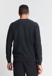 Zwarte lange mouwen trui met een ronde hals, ribbelmanchetten en -zoom, gemaakt van een zachte textuurstof, gezien van achteren.