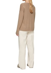 Beige Strickpullover mit lockerer Passform und geripptem Saum, kombiniert mit off-white weiten Hosen, die eine sanfte Textur und neutrale Farben präsentieren.