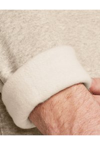 Lys grå sweatshirtærme med en blød, hvid fleecekant. Nærbillede viser struktureret strikstof og glat fleece-detalje.