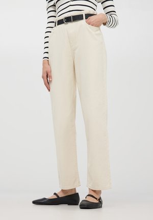 Pantaloni beige a vita alta con taglio dritto, dotati di tasche laterali e una cintura nera in evidenza, abbinati a scarpe basse nere.