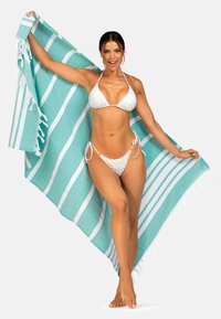 Biały bikini z wirującymi wzorami i majtkami wiązanymi po bokach, zestawione z dużym, turkusowo-białym ręcznikiem plażowym w paski z frędzlami.