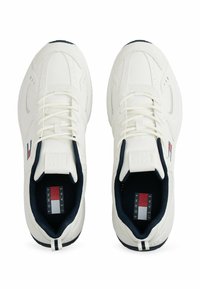 Chaussures de sport blanches avec une tige synthétique lisse, doublure bleu marine et accent rayé sur le talon. Elles présentent des lacets plats et des détails de logo.