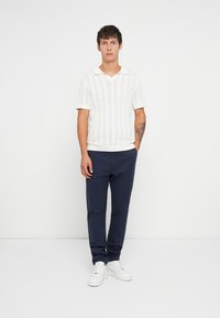 Polo a maglia bianca con maniche corte, abbinato a pantaloni blu navy e sneakers bianche. Tessuto semplice e traspirante con una vestibilità casual.