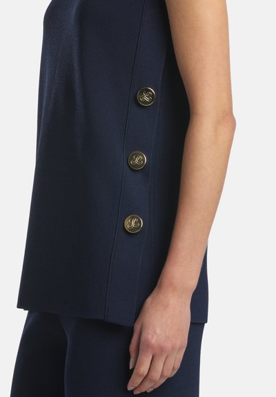 Haut sans manches bleu marine avec trois boutons décoratifs dorés sur le côté, porté avec un pantalon bleu marine assorti.