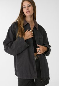 Overmaatse donkergrijze jas met een bruine corduroy kraag, voorrits, zijzakken en een relaxte pasvorm. Geschikt voor casual dragen.