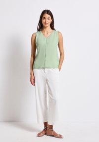 Haut sans manches vert clair avec un décolleté en V et un ourlet droit, associé à un pantalon large blanc et des sandales argentées à lanières.