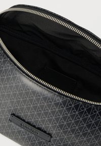 Schwarzes Täschchen mit gemustertem Äußeren, kleinen grauen Herzen, silbernem Reißverschluss und schwarzer Innenausstattung. Markenetikett innen.