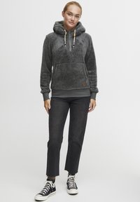 Grijze fleece hoodie met een voorzak, een capuchon met trekkoord en houten accenten. Combinatie met zwarte cropped jeans en zwarte sneakers.