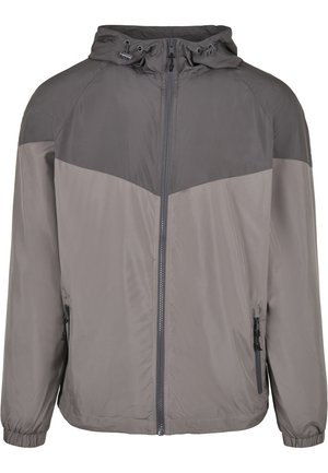 Jachetă gri tip windbreaker cu o yoke contrastantă de un gri închis, închidere cu fermoar, glugă ajustabilă și manșete elastice. Include buzunare laterale cu fermoar.