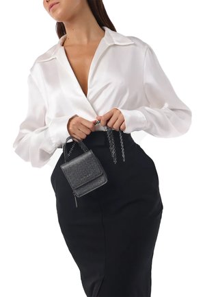 Schwarze Tasche mit Kettenhenkel, strukturierter grauer Stoff. Das Model trägt ein weißes Satin-Shirt und einen schwarzen, hochgeschnittenen Rock.