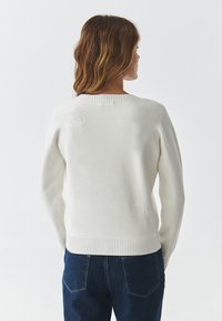 Suéter blanco de punto con cuello y puños acanalados. Presenta diseños tonales de Mickey Mouse y Donald Duck en la parte trasera. Corte casual.