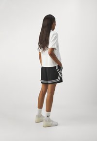 White t-shirt with short sleeves, paired with black shorts featuring white trim, worn with white sneakers and crew-length socks.