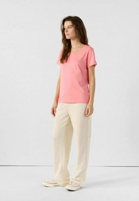 Camiseta de algodón de color rosa con mangas cortas, combinada con pantalones de pierna ancha de color crema. Diseño simple sin patrones ni acentos.