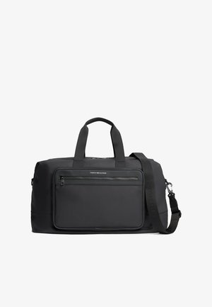 Bolsa de viaje de nailon negra con asas dobles, correa de hombro ajustable, bolsillo frontal con cremallera y detalle de logo. Textura suave, forma rectangular.