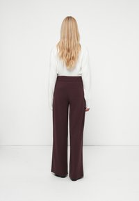 Pantalones de pierna ancha burdeos con una textura suave y cinturilla elástica, combinados con una camiseta de manga larga blanca, vistos desde la parte posterior.
