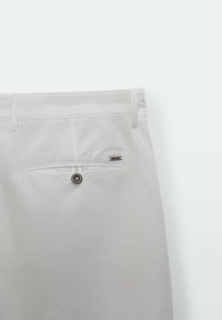 Pantalon blanc en coton avec une poche arrière à bouton, des coutures surpiquées et une texture lisse, agrémenté d'un petit logo métallique.