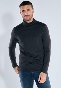 Schwarzer Rollkragenpullover mit langen Ärmeln, glatter Textur, tailliertem Design und hohem Kragen. Kombiniert mit blauen Jeans.