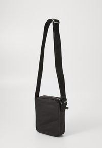 Sac bandoulière noir avec une forme rectangulaire, en tissu lisse, fermeture éclair et sangle tissée ajustable. Design simple avec des accents minimalistes.