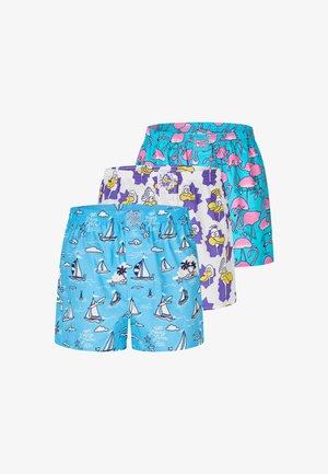 Muskelbepackter Mann mit kurzen geflochtenen Haaren trägt hellblaue Badeshorts mit weißen und dunkelblauen Segelboot- und Wolkenmustern, der vor einem schlichten Hintergrund steht.