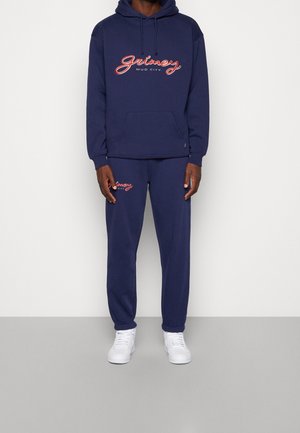 Marineblaues Hoodie- und Sweatpants-Set, aus weichem Stoff gefertigt. Mit weißem und rotem "Grimey Mud City"-Logo, Kängurutasche und elastischen Bündchen.