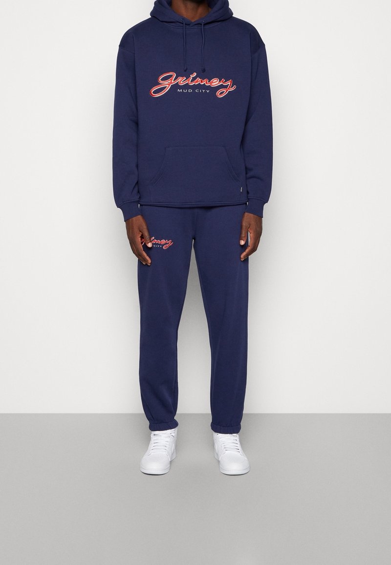 Mörkblå hoodie och sweatpants-set, tillverkat av mjukt tyg. Utrustat med vit och röd "Grimey Mud City" logotyp, med känguruficka och elastiska mudd.