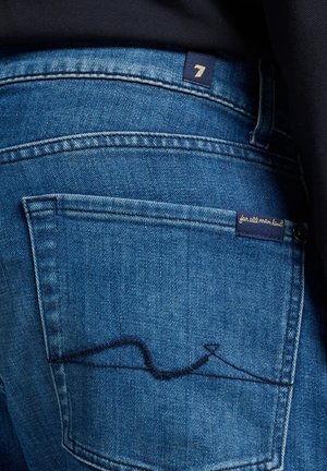 Dark blue denim jeans with a visible back pocket featuring unique stitching. Includes a label with "7" and "for all mankind."