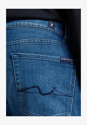 Granatowe dżinsy z widoczną tylnią kieszenią z unikalnym przeszyciem. Zawierają metkę z napisem "7" oraz "for all mankind."